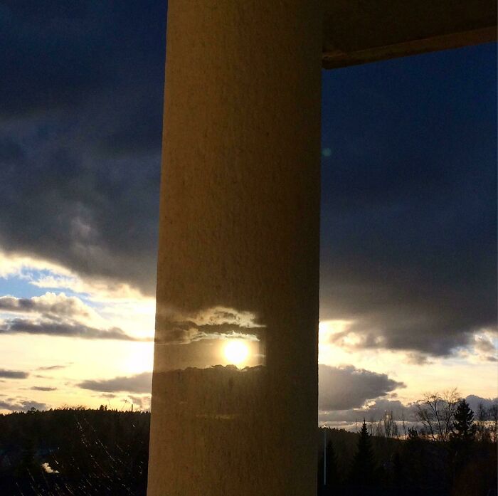 Image Reflected From Double Glazing Window Is Aligned With A Real Image Of Sun And Clouds Behind The Pillar