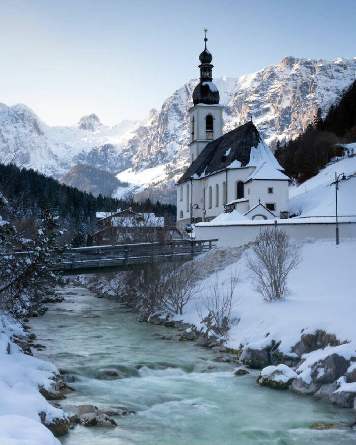 Snow-covered castle near a flowing river with mountains in the background, showcasing beautiful castles around the world.