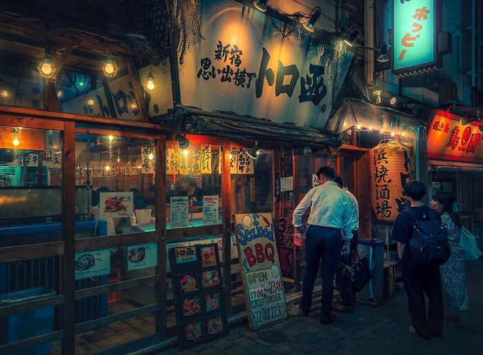 Street scene in Japan at night with people outside traditional restaurants, capturing the beauty of Japan in vibrant colors.