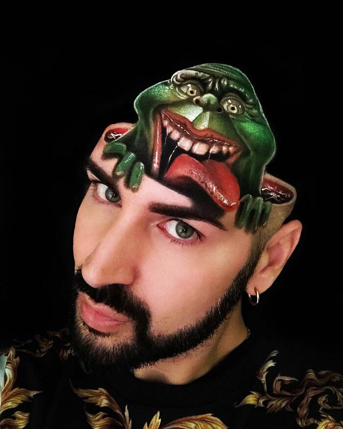 Man with optical illusion body painting of a green creature on his head by Italian artist using his body as a canvas.