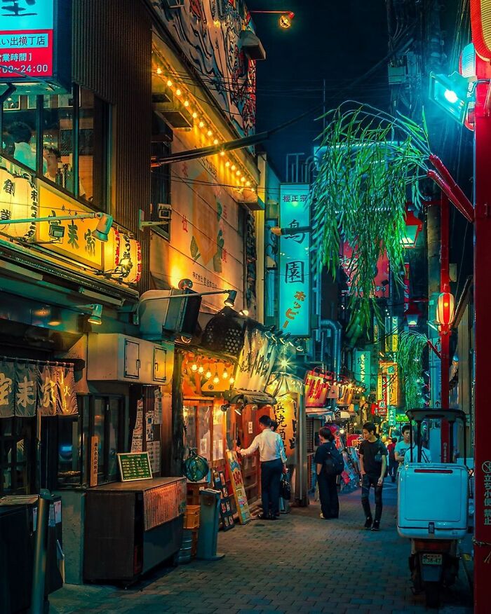 Vibrant night street scene in Japan with illuminated signs, local shops, and people walking along a lively alleyway.