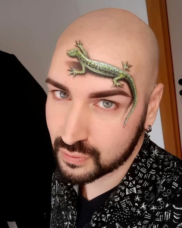 Italian artist with a realistic lizard body painting creating a convincing optical illusion on his bald head.