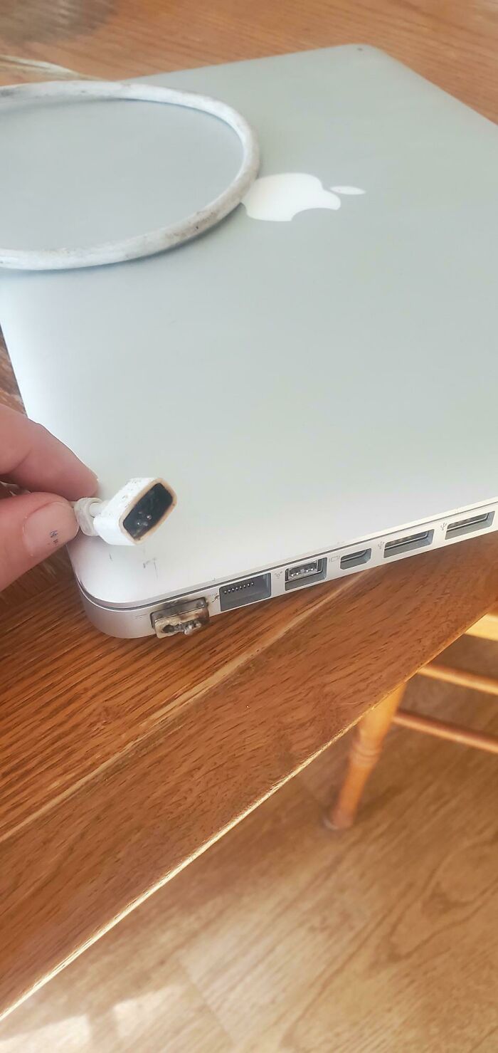 A damaged MacBook with a burnt charging port and a frayed MagSafe cable showing a common tech support worst case.