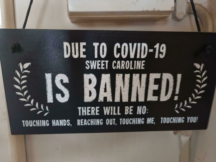 Funny sign humorously banning "Sweet Caroline" due to COVID-19 with playful text about touching.