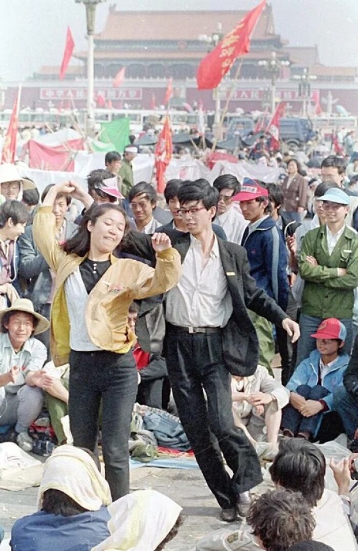Couple dancing amidst a crowd in a historical protest, highlighting cultural change and historical significance.
