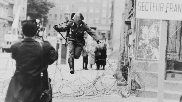 A soldier jumps over barbed wire at the Berlin Wall, captured in a significant historical photo.