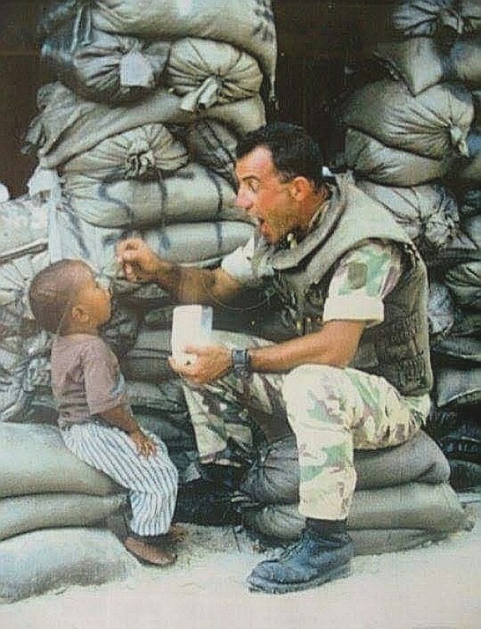 Soldier feeding a child in front of sandbags, showcasing important historical moments that change perspectives.