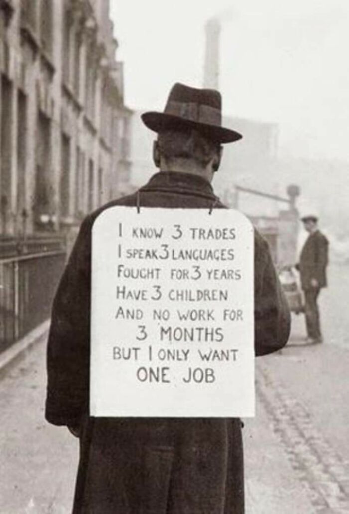 Man in historical photo wearing placard seeking work, illustrating economic hardship and resilience.