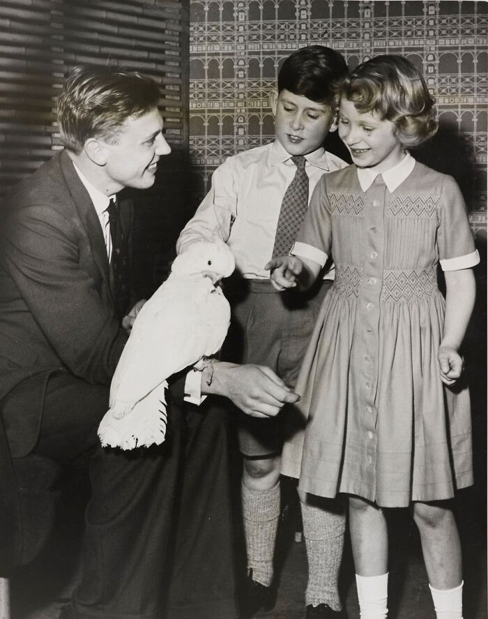 Man with historical significance interacts with children, holding a cockatoo, in a vintage photo setting.