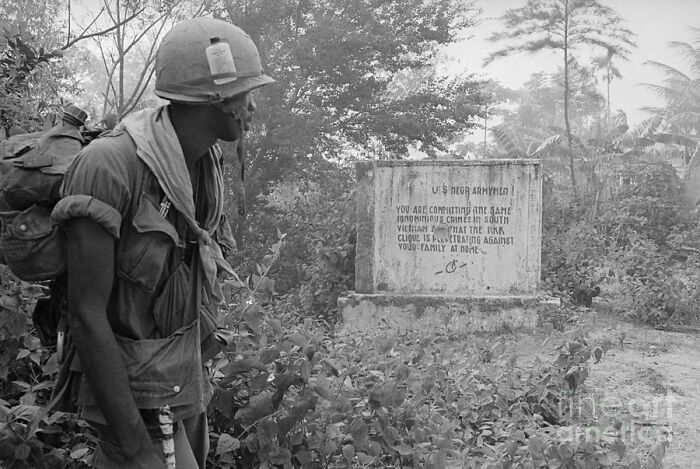 Soldier in helmet observing a warning sign in the jungle during a historical military conflict.