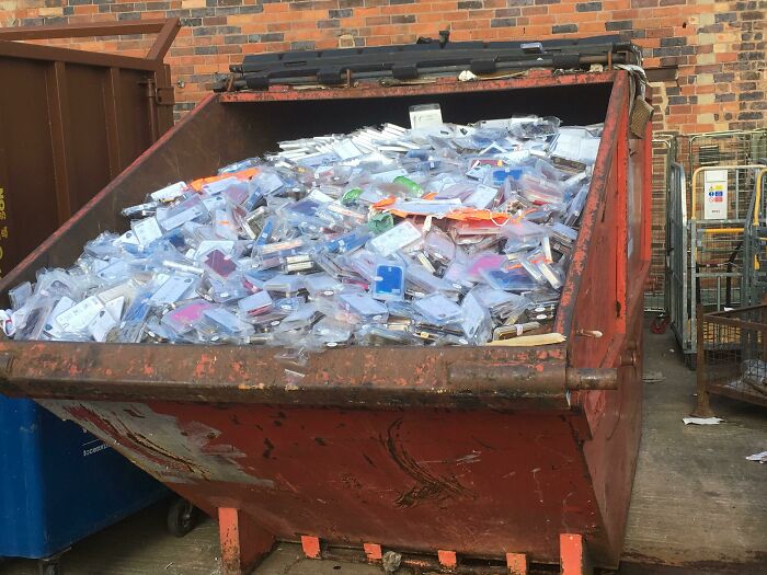 Dumpster overflowing with discarded plastic packaging, illustrating waste and anti-consumption themes in an urban setting.
