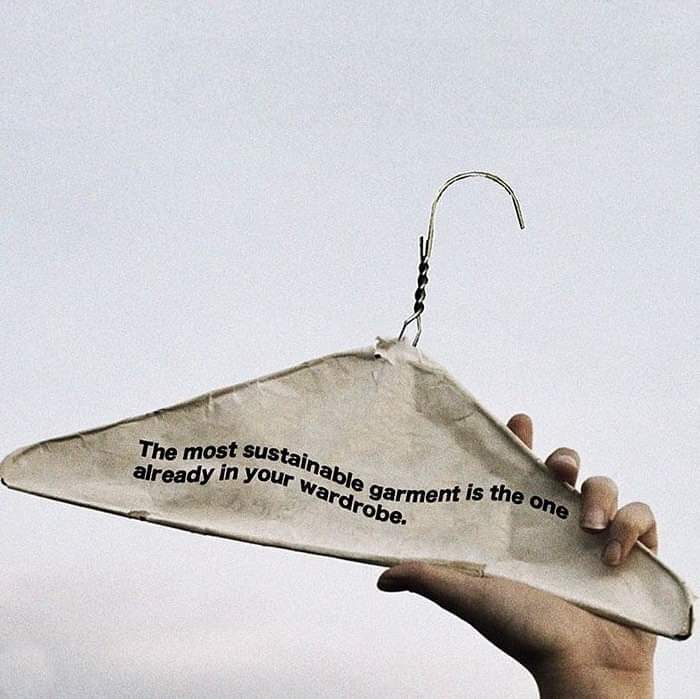 Hand holding a worn clothes hanger with message promoting anti-consumption and sustainability in fashion.