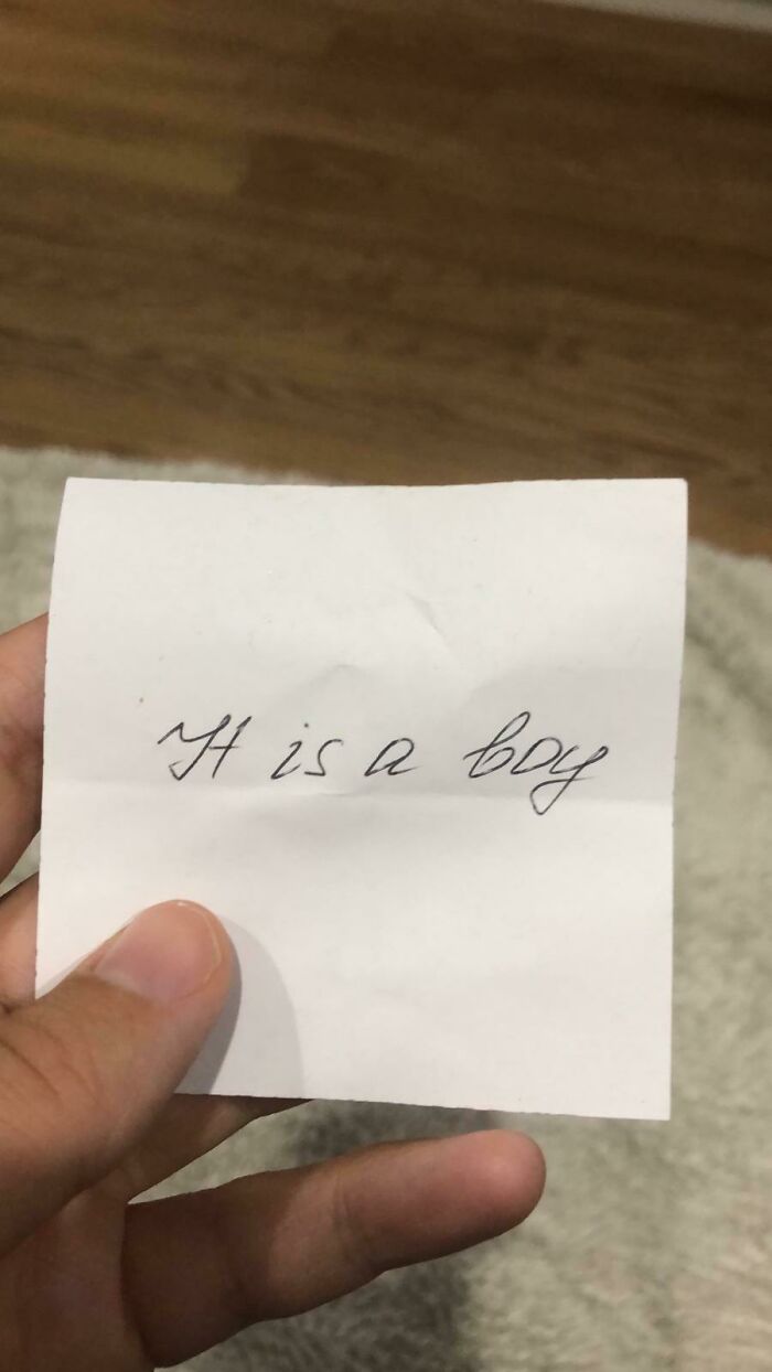 Hand holding a handwritten note with the phrase it is a boy, reflecting anti-consumption humor.