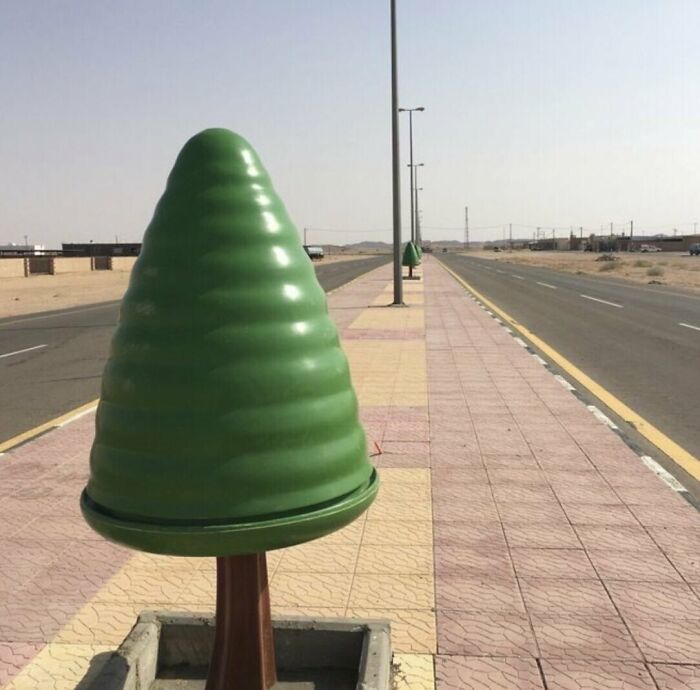 Green cone-shaped objects installed on a sidewalk in an empty urban area illustrating urban hell and dystopian cityscape.