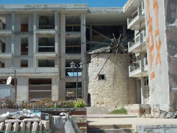 Old stone windmill surrounded by unfinished, abandoned buildings illustrating urban hell dystopian scenes.