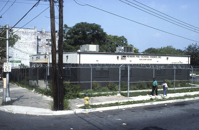Chain-link fence topped with barbed wire surrounds a rundown urban building, illustrating urban hell in a dystopian setting.