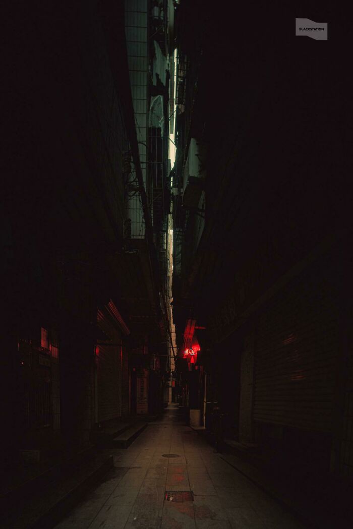 Dark narrow urban alley with dim lighting and red neon signs, depicting a real-life urban hell scene.
