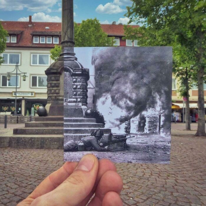 Black and white war photo held against a modern city square showing then and now contrast of time changes.