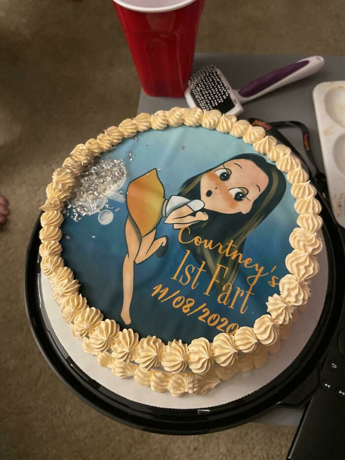 Funny cake fail with a cartoon image and the text "Courtney's 1st Fart", surrounded by decorative icing.