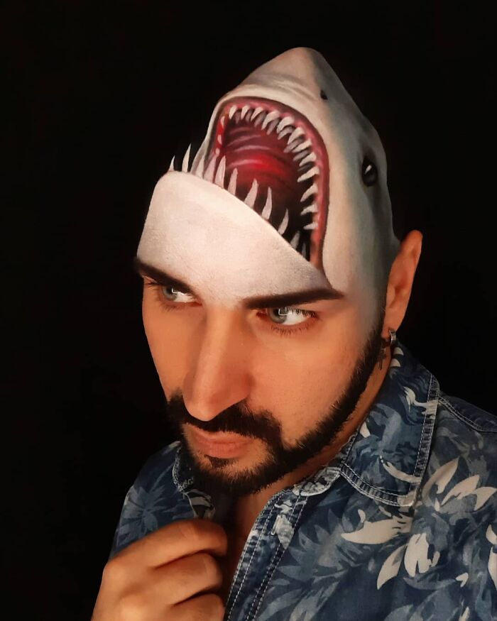 Man with body art on his head showing a shark mouth, an optical illusion by Italian artist using his body as canvas.