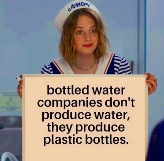 Person in sailor hat holding sign with anti-consumption message about bottled water companies producing plastic bottles.