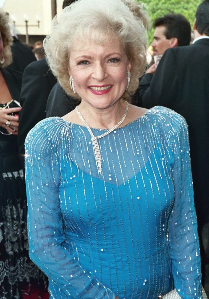 Smiling elderly woman in a blue sequined dress and diamond jewelry at a formal event, capturing not-so-fun facts online group.
