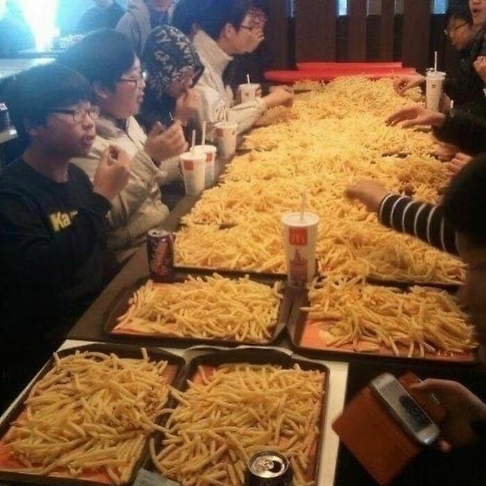 Group of people sitting at a long table covered with trays filled with a massive amount of French fries from Instagram account.
