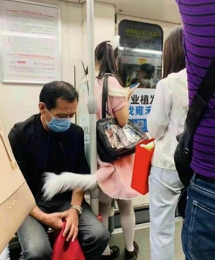 Man wearing a face mask sitting on subway with a fake animal tail attached to a woman's bag, highlighting weird Instagram account content.