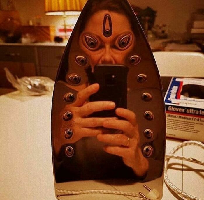 Person taking selfie reflected on a distorted iron surface creating a surreal and weird Instagram account image effect.