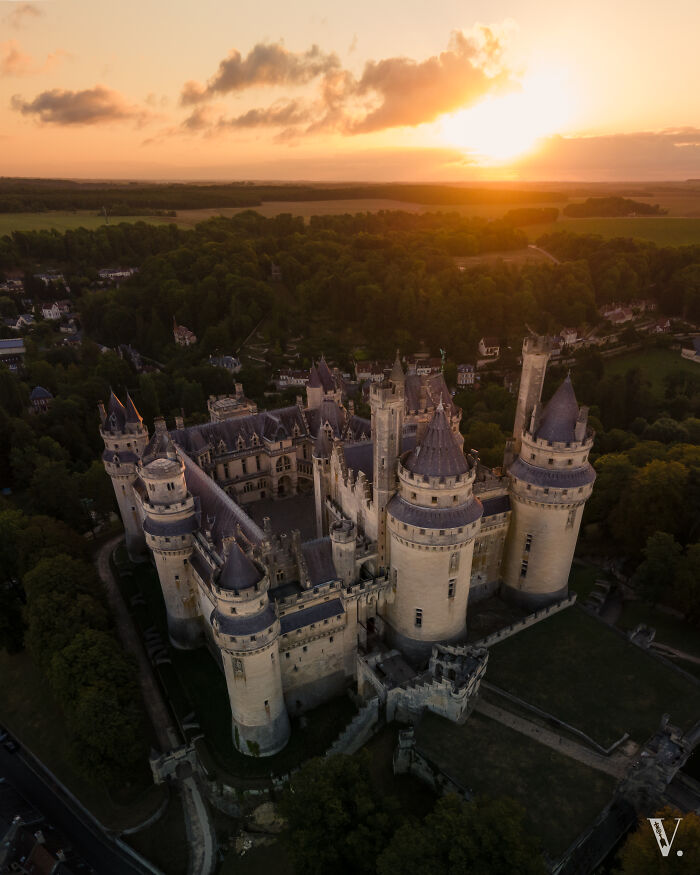Aerial view of a beautiful castle surrounded by trees at sunset showcasing stunning architecture and historic charm.
