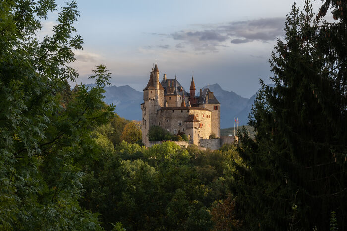 Medieval castle surrounded by lush greenery with mountains in the background, showcasing beautiful castles around the world.