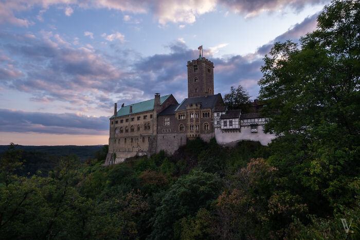 Medieval castle atop a lush hill surrounded by trees under a dramatic evening sky, showcasing beautiful castles around the world.