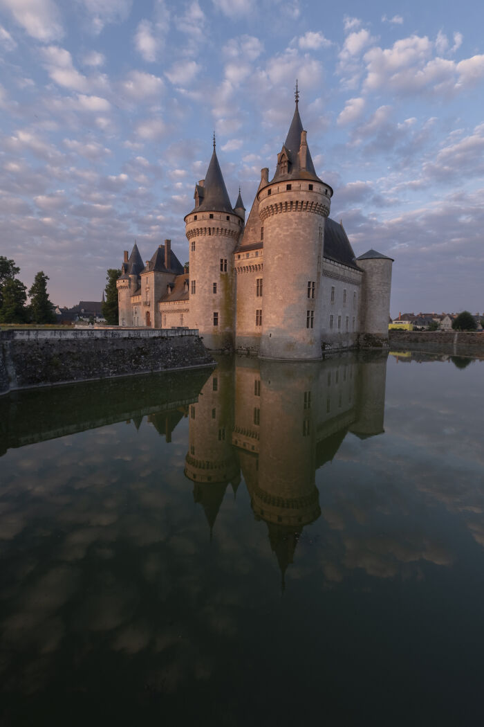 Historic castle with turrets surrounded by water reflecting the sky, showcasing one of the most beautiful castles around the world.