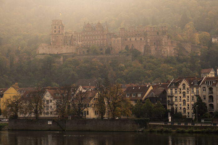 Historic castle surrounded by autumn foliage overlooking a river and charming village, showcasing beautiful castles around the world.