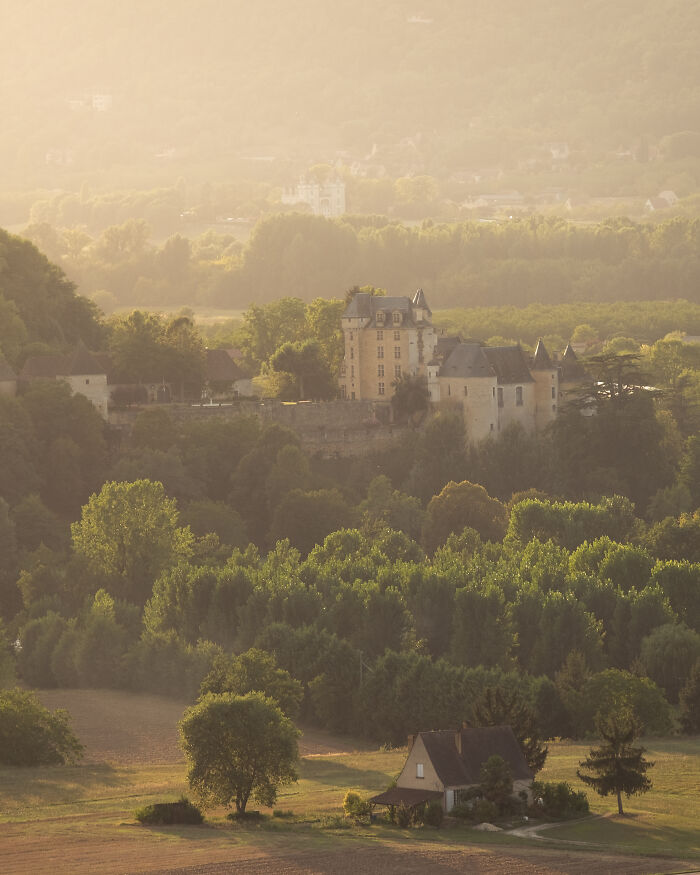 Beautiful castle surrounded by lush greenery and hills, captured in soft golden light showcasing stunning architecture.