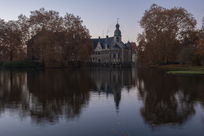 Historic castle with classic architecture reflecting in calm water surrounded by autumn trees under a dusky sky
