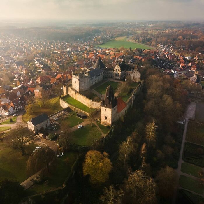 Aerial view of a beautiful castle surrounded by trees and a village, showcasing stunning architecture and historic walls.