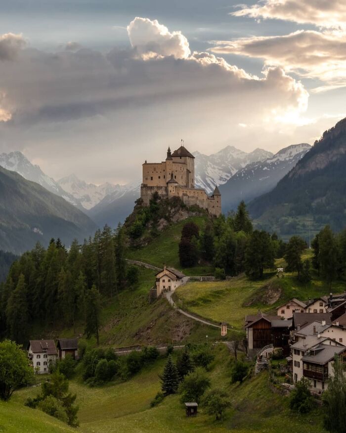 Medieval castle perched on a hill surrounded by alpine forest and snow-capped mountains capturing beautiful castles worldwide.