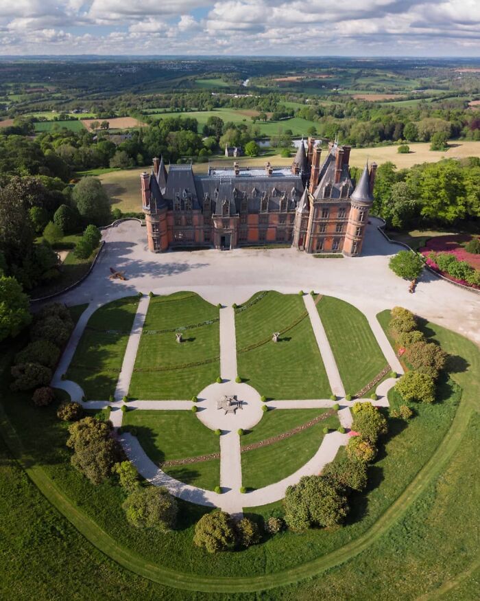 Aerial view of a beautiful historic castle surrounded by manicured gardens and lush green landscape.