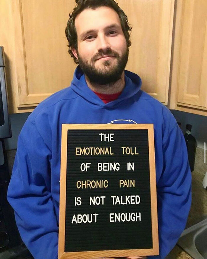 Man in blue hoodie holding sign about the emotional toll of chronic pain raising chronic illness awareness