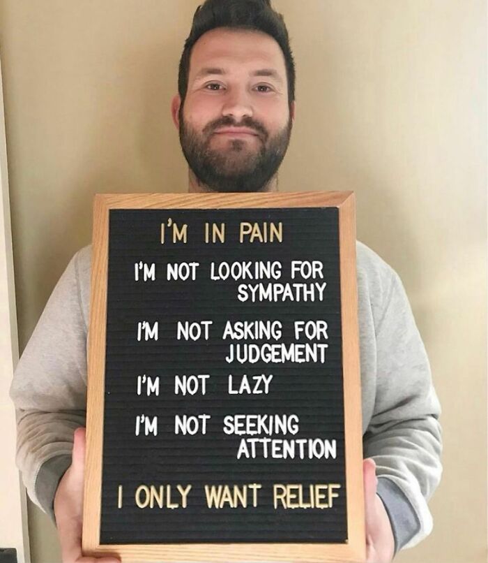 Man holding sign about pain and relief, spreading awareness about what people with chronic illnesses experience daily.
