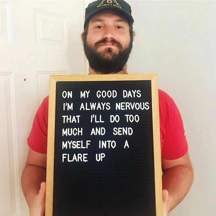 Man in a red shirt holding a sign about chronic illness flare ups, spreading awareness of daily struggles.