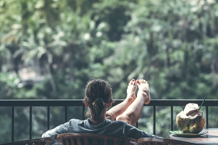 Person relaxing on a balcony with feet up, enjoying a peaceful view, showcasing subtle signs of wealthy lifestyle.