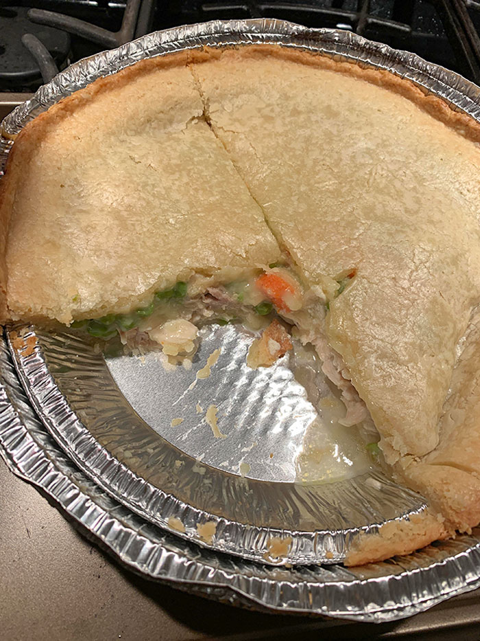 Partially eaten homemade chicken pot pie with vegetables in a foil baking dish showing misleading portion size marketing technique.