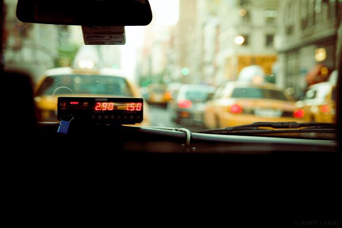 Taxi meter inside a cab with blurred yellow taxis and city street visible through the windshield.