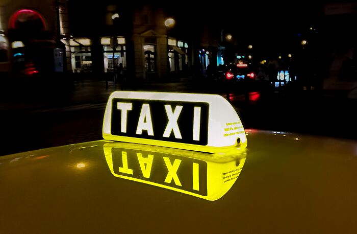 Yellow taxi sign lit on car roof at night reflecting on the surface, representing taxi and Uber drivers' roadside experiences.