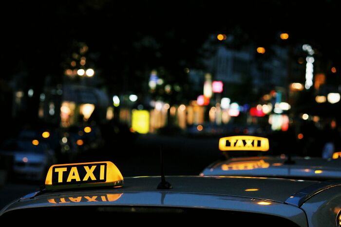 Taxi and Uber drivers waiting at night with illuminated taxi signs on car roofs in a blurred city street scene.