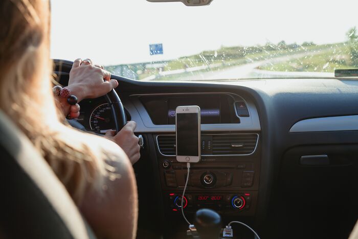 Taxi and Uber driver gripping steering wheel in car interior with smartphone mounted while driving on highway.