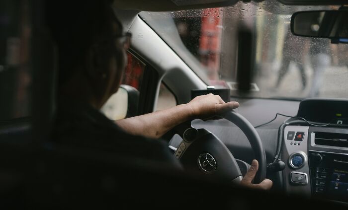 Taxi driver gripping steering wheel inside car during rainy weather, illustrating experiences of taxi and Uber drivers.