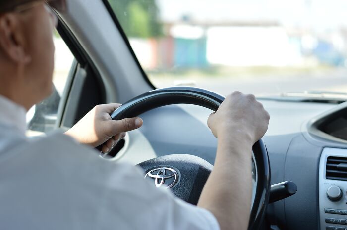 Taxi and Uber driver gripping steering wheel while navigating city streets during a daytime ride.